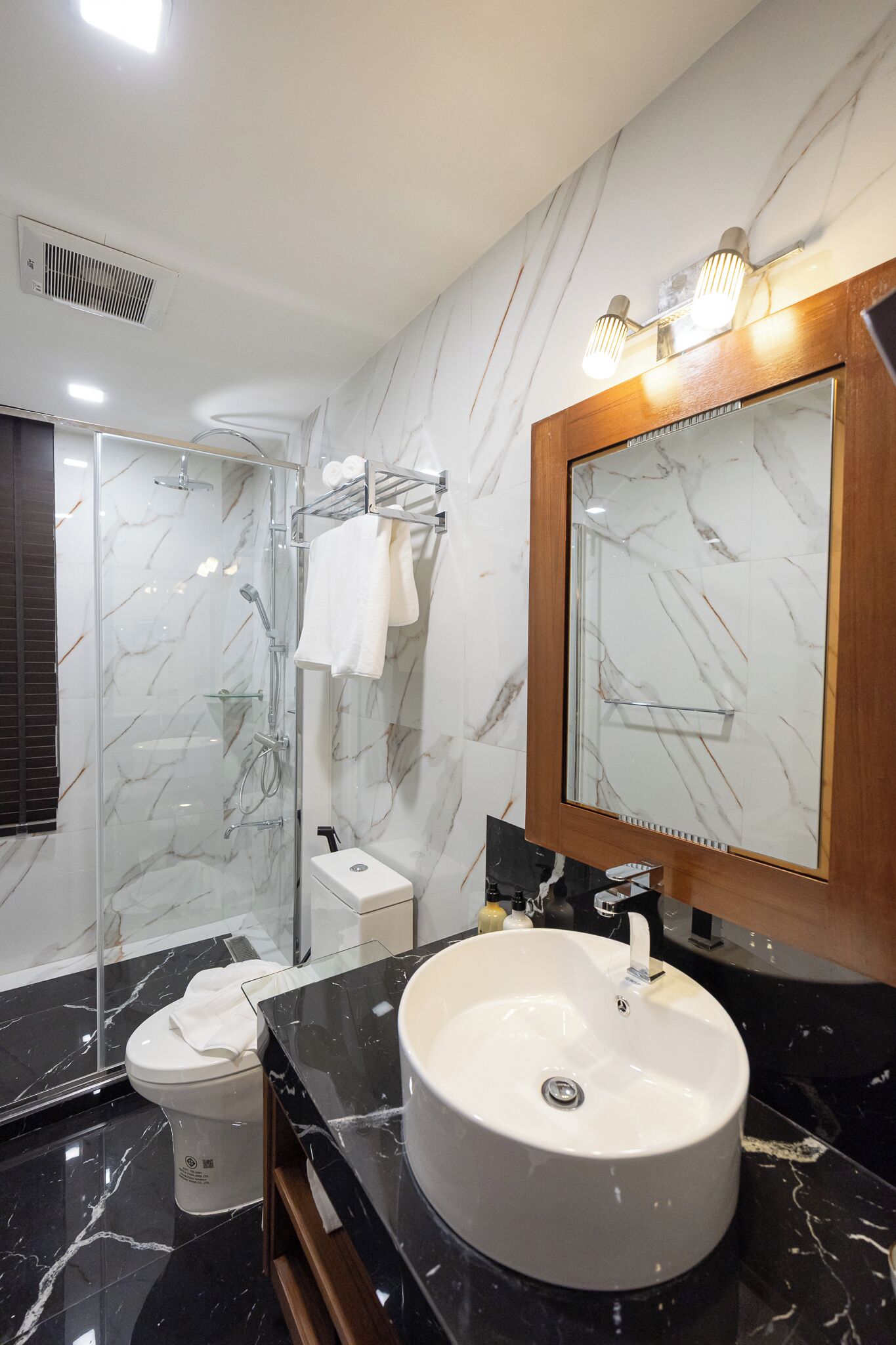 A modern bathroom with a marble vanity, a large mirror, a glass shower enclosure, and a toilet.