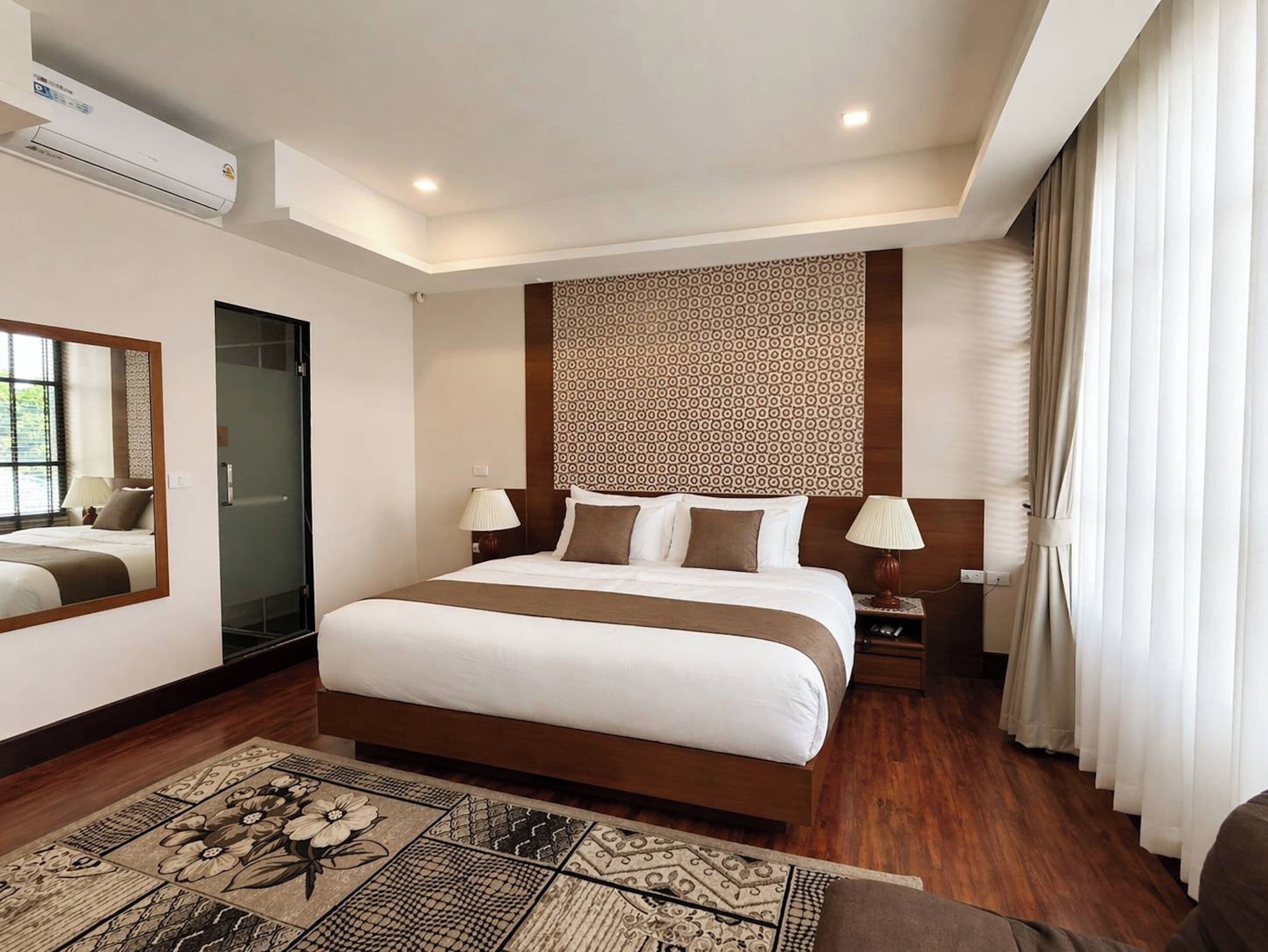 A hotel room with a large bed, bedside lamps, a mirror, a patterned wall, and a window with curtains.