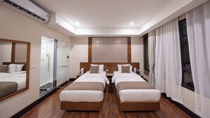 Una camera d'albergo con due letti singoli, un grande specchio, una doccia e un poggiatesta decorato.