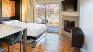 A hotel room with a bed, a dining table, a TV, a fireplace, and a view of the desert landscape. - Cozy studio condo in Moab during Music Festival (Moab)