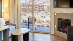 A modern living room with a fireplace, a sofa, a coffee table, and a view of a desert landscape through large sliding doors. - Cozy studio condo in Moab during Music Festival (Moab)