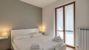 Ein Schlafzimmer mit Bett, Nachttischlampen, einem Heizkörper und einem Fenster mit Jalousien.