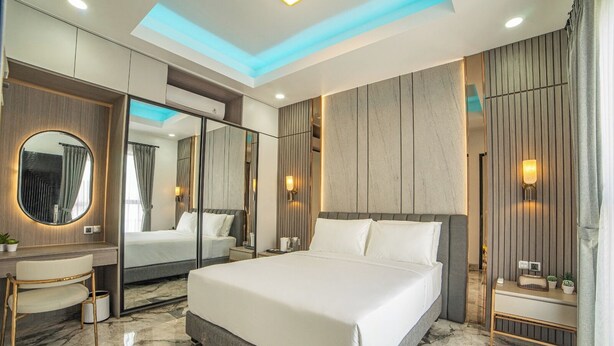 A modern hotel room with a large bed, a vanity with a mirror, and a seating area. - Bellagio Villas (Denpasar)