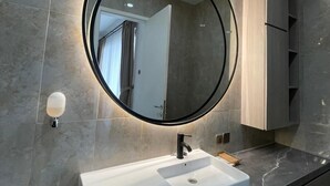 A modern bathroom with a round mirror, white sink, and grey tiles. - Bellagio Villas (Denpasar)