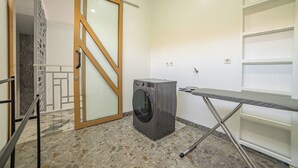 A laundry room with a washing machine, ironing board, and a sliding glass door leading to a staircase. - Bellagio Villas (Denpasar)