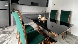 A modern kitchen with a dining area, featuring a black glass table, green upholstered chairs, and marble flooring. - Bellagio Villas (Denpasar)