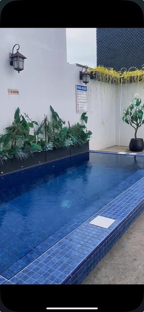 Piscina con piastrelle blu, circondata da vasi con piante e un cartello 'No Smoking'.
