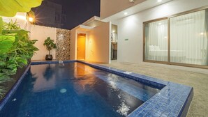 A swimming pool with a tiled edge, surrounded by plants and a building with a balcony. - Bellagio Villas (Denpasar)