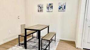 A room with a wooden table and bench, white walls, and three abstract paintings on the wall. - Cozy-King Bed Apt in peaceful Spring-Woodlands (Spring)