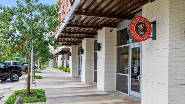 Un restaurant Chipotle Mexican Grill doté d’une terrasse couverte, d’une façade en briques et d’un trottoir bordé d’arbres et de bancs.