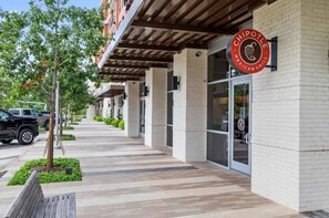 Ein Chipotle Mexican Grill mit überdachter Außenbestuhlung, einer Ziegelhausfassade und einem Bürgersteig mit Bäumen und Bänken.