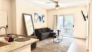 Un salon moderne avec un coin cuisine, un grand miroir, un canapé gris et un balcon avec vue.