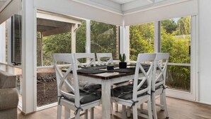A covered patio with a table and chairs, large windows, and a view of greenery. - Buttercup cottage, Rye (Rye)