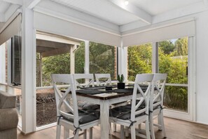 A covered patio with a table and chairs, large windows, and a view of greenery. - Buttercup cottage, Rye (Rye)