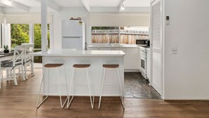 A modern kitchen with a central island, white cabinetry, and a dining area with a table and chairs. - Buttercup cottage, Rye (Rye)