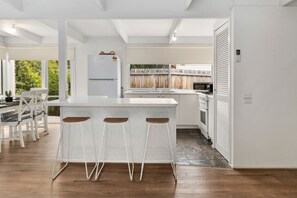 A modern kitchen with a central island, white cabinetry, and a dining area with a table and chairs. - Buttercup cottage, Rye (Rye)