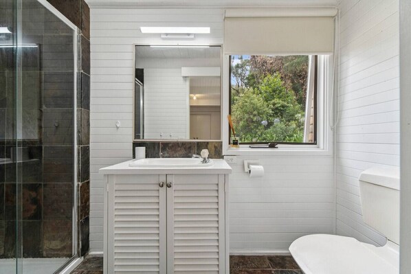 A bathroom with a white vanity, a glass shower enclosure, and a window with a view of greenery. - Buttercup cottage, Rye (Rye)