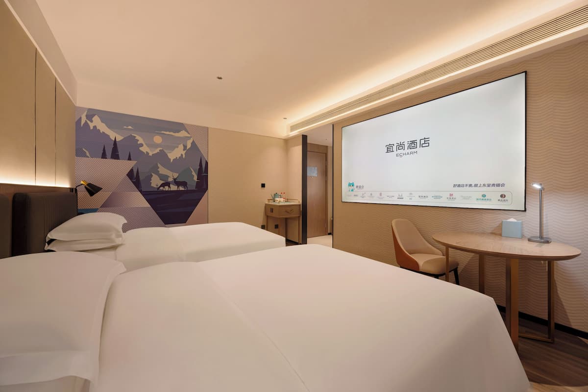 Habitación de hotel con dos camas, un escritorio y una pantalla grande que muestra información de la habitación.