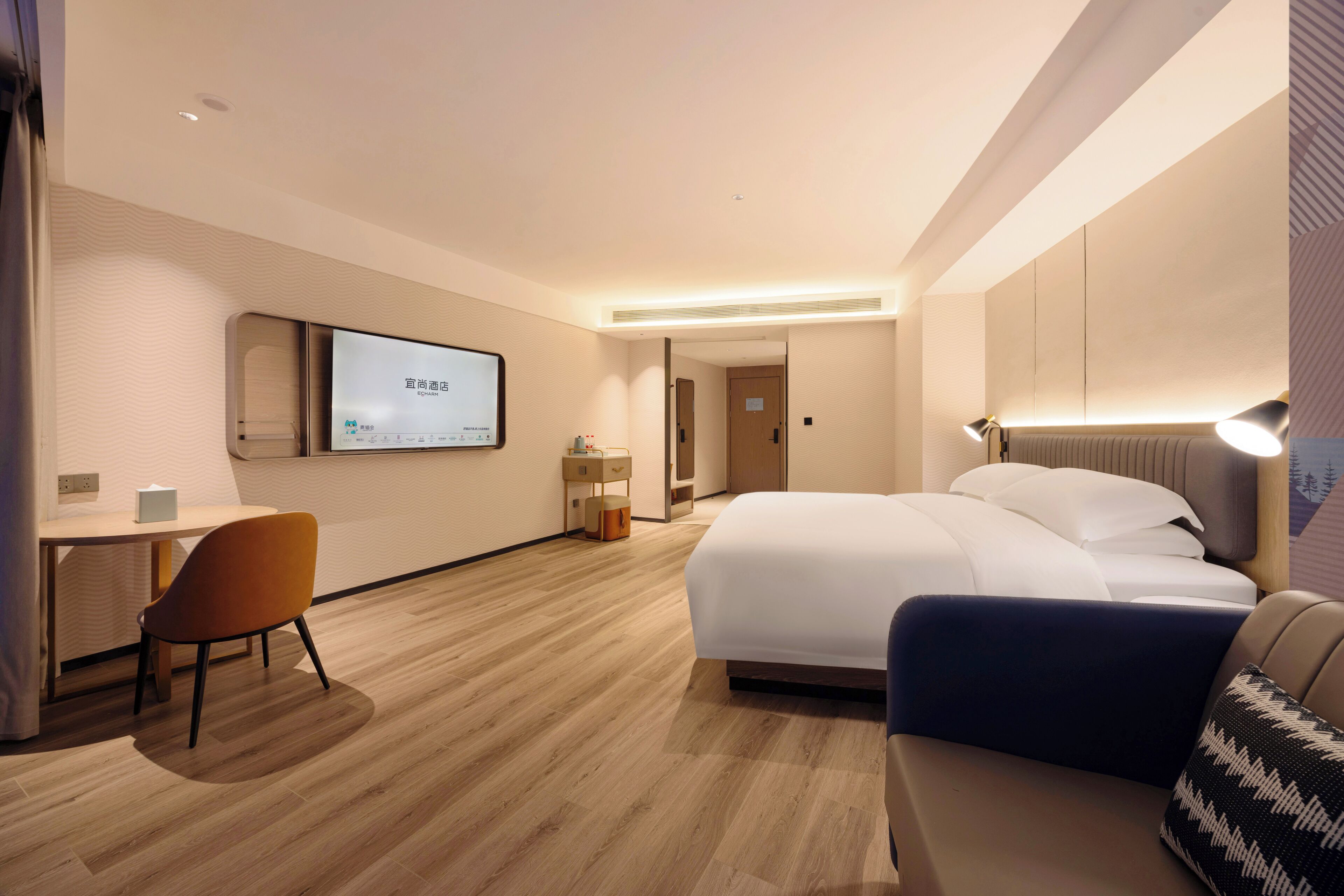 A modern hotel room with a bed, a desk, a chair, and a TV on the wall.