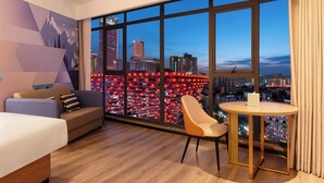 A modern hotel room with a large window offering a city view, a sofa, a bed, and a small table. - Echarm Hotel JiefangbeiPedestrianStreet  (Chongqing)