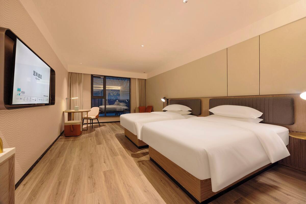 Habitación de hotel con dos camas, un escritorio, una silla y un ventanal grande.