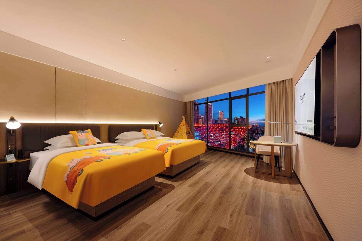 Habitación de hotel con dos camas, un escritorio y un amplio ventanal con vistas a la ciudad.