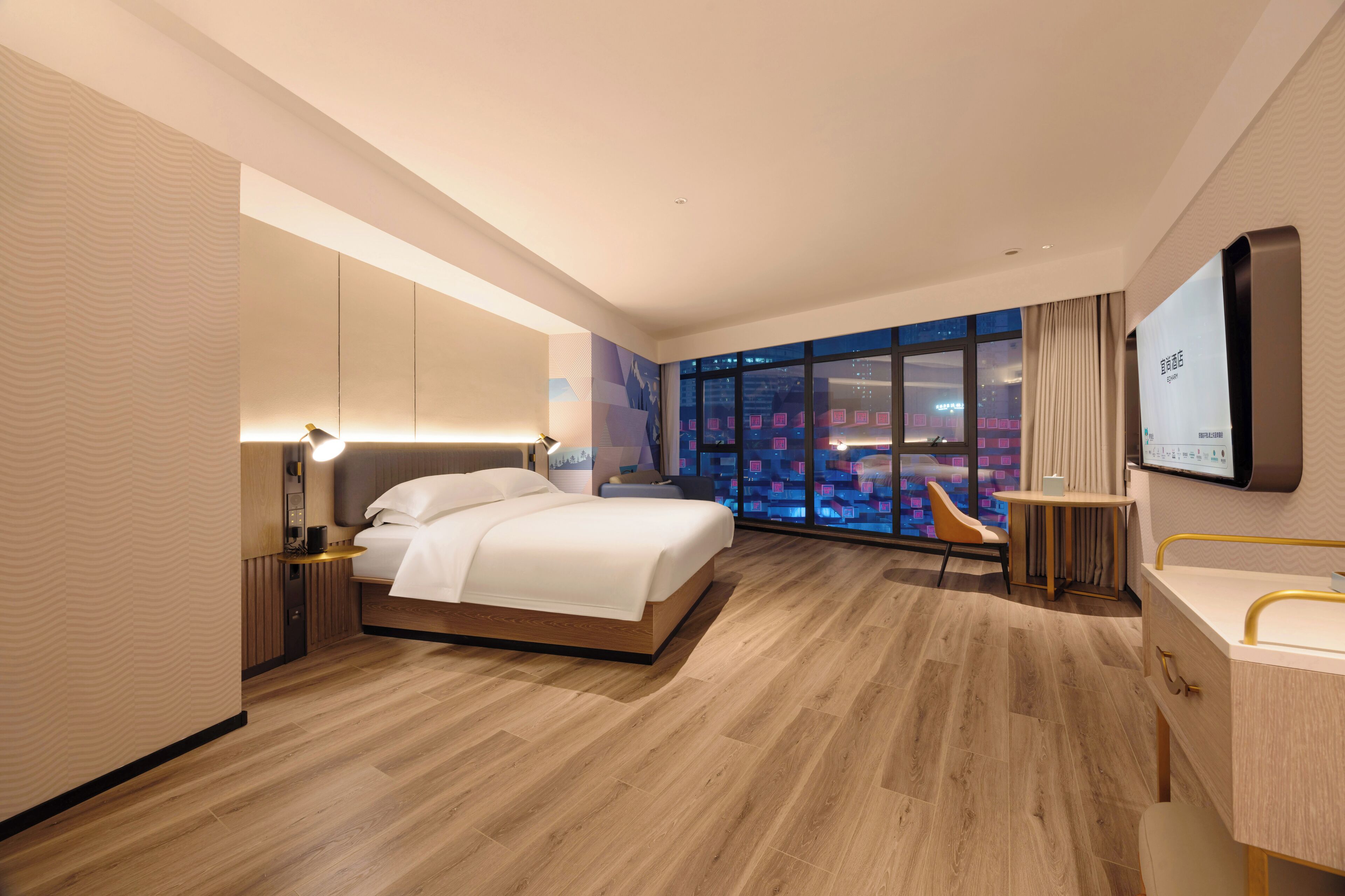 A modern hotel room with a large bed, a desk with a chair, a TV mounted on the wall, and a large window with a city view.