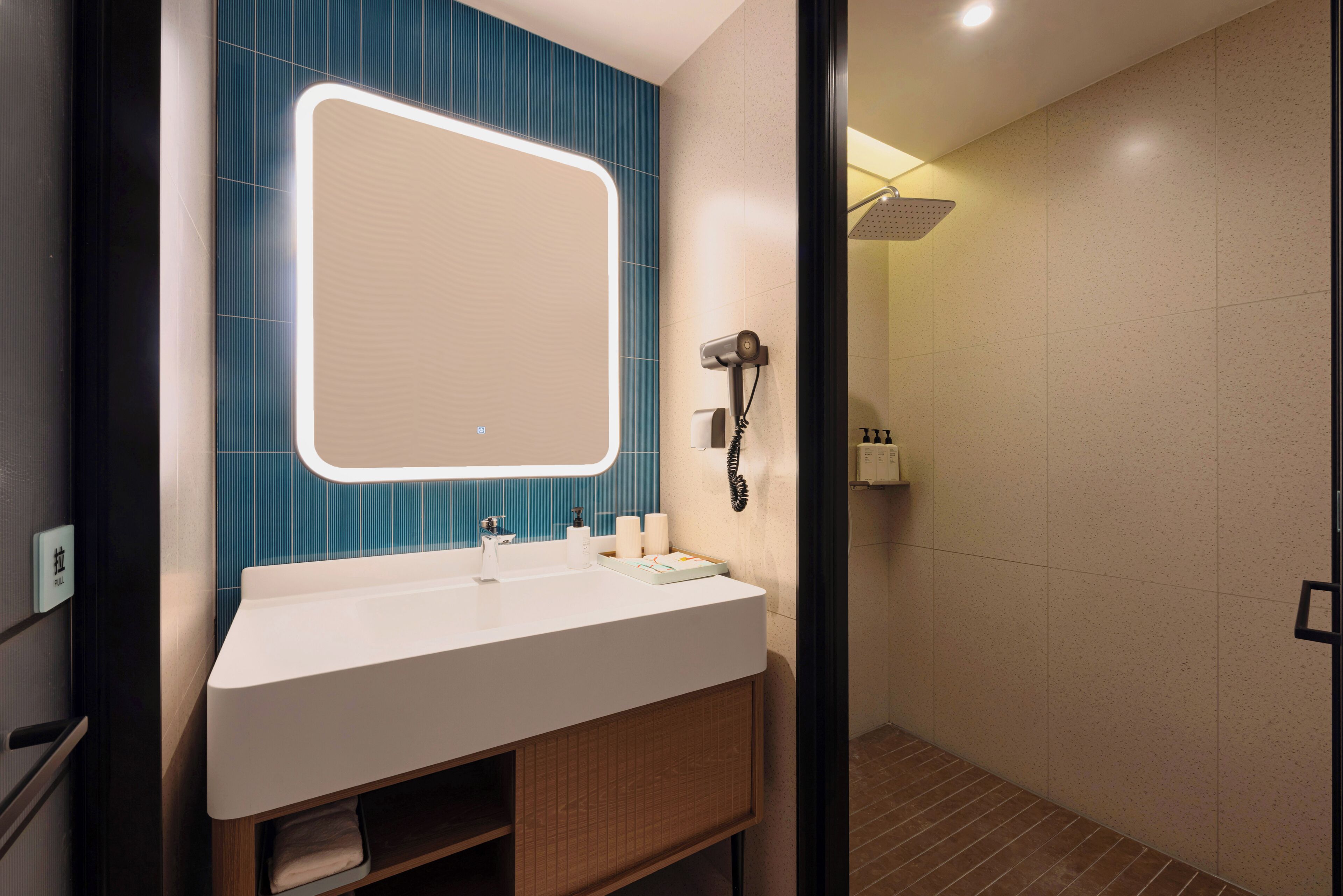 Une salle de bain moderne avec un lavabo blanc, un mur recouvert de carreaux bleus et une douche séparée par une paroi en verre.