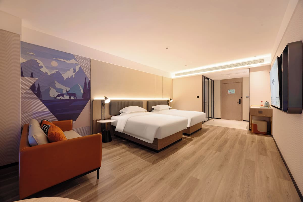 Una habitación de hotel moderna con dos camas, un sofá, un cuadro y un televisor.