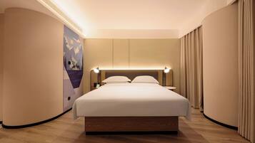 A modern hotel room with a large bed, a headboard with integrated lighting, a wall mural, and a curved ceiling.