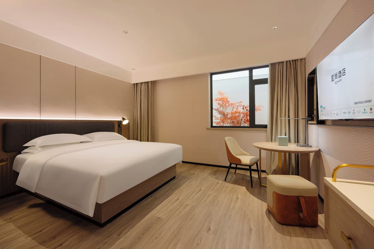 Una habitación de hotel moderna con una cama grande, un escritorio, una silla y una pantalla de televisión.
