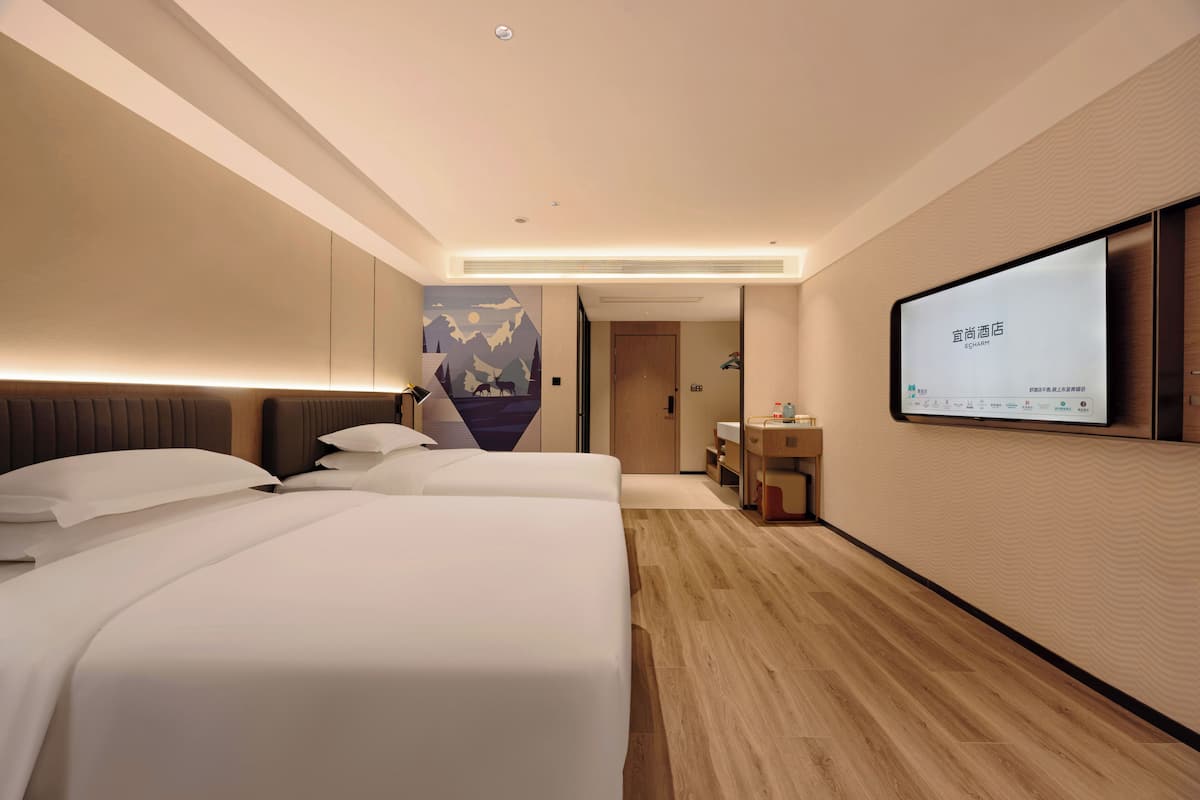 Habitación de hotel con dos camas, una televisión de pantalla plana, piso de madera y una obra de arte colgada en la pared.