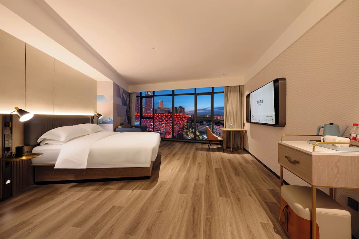 Una habitación de hotel moderna con una cama grande, un escritorio, una silla y un televisor en la pared.
