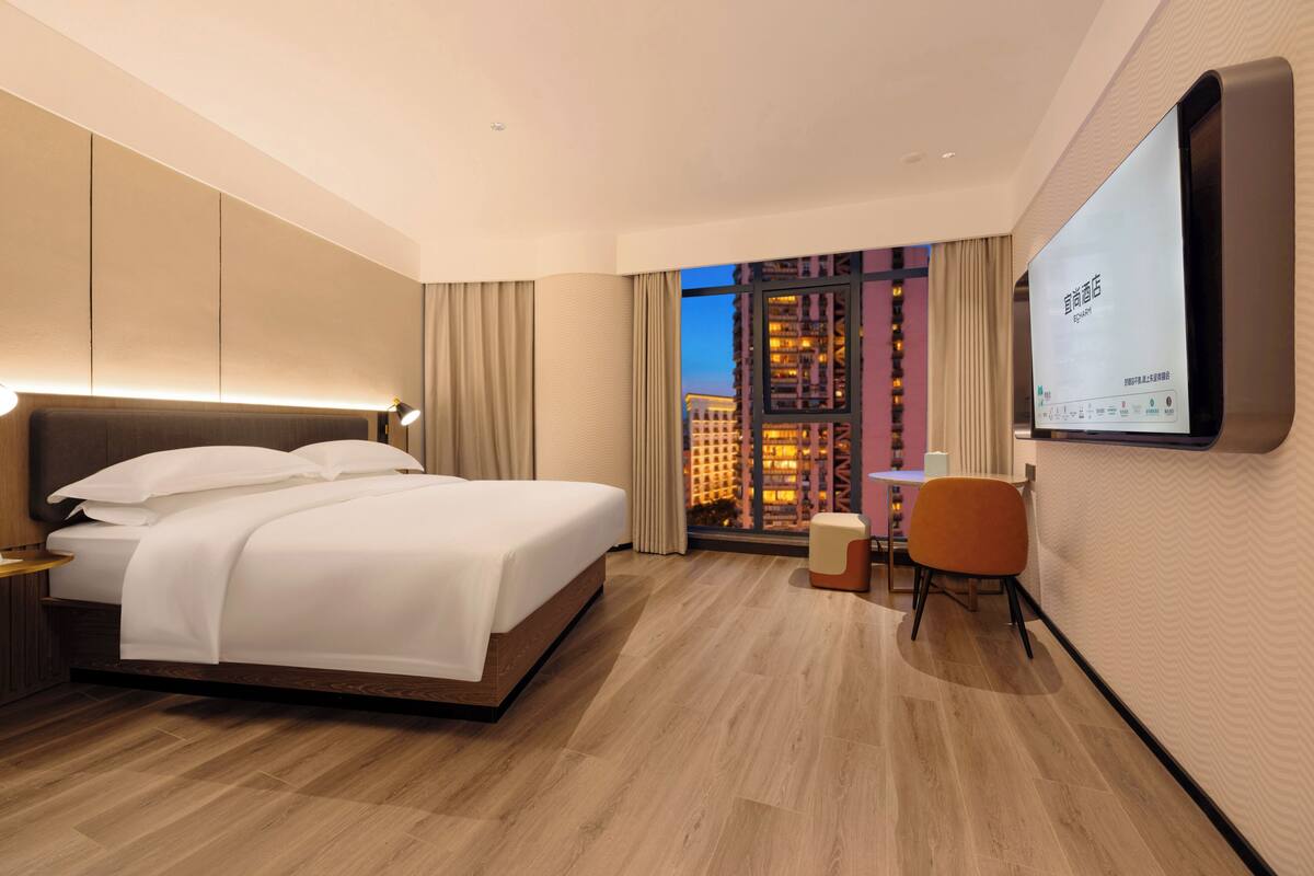 Una habitación de hotel moderna con una cama grande, un escritorio y un televisor montado en la pared.