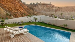 A swimming pool with lounge chairs, a table, and small plants. - ELIVAAS Luxe Shourya Eden 3 BHK villa  (Udaipur)
