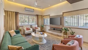A modern living room with a green sofa, pink armchairs, a white coffee table, and a flat-screen TV mounted on the wall. - ELIVAAS Luxe Shourya Eden 3 BHK villa  (Udaipur)