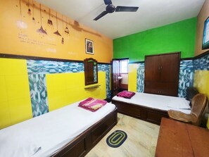 A room with two beds, a wooden chair, a ceiling fan, and a mirror on the wall. - Hotel Sushil International (Kolkata)