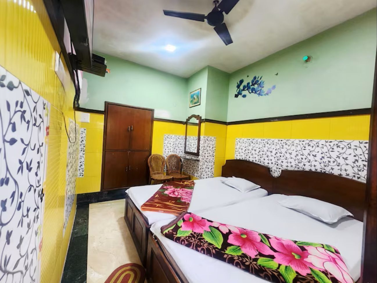 A bedroom with a bed, a ceiling fan, a wooden wardrobe, and a chair.