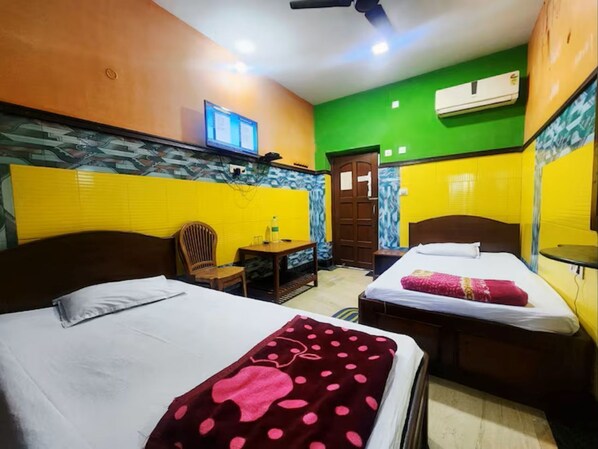 Quarto de hotel com duas camas, uma mesa pequena, uma cadeira e um aparelho de ar condicionado.