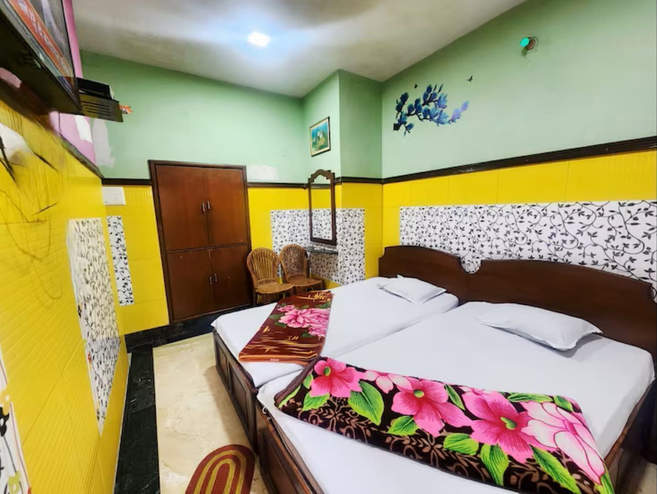 A hotel room with a bed, a wardrobe, a chair, and a wall with a floral pattern.