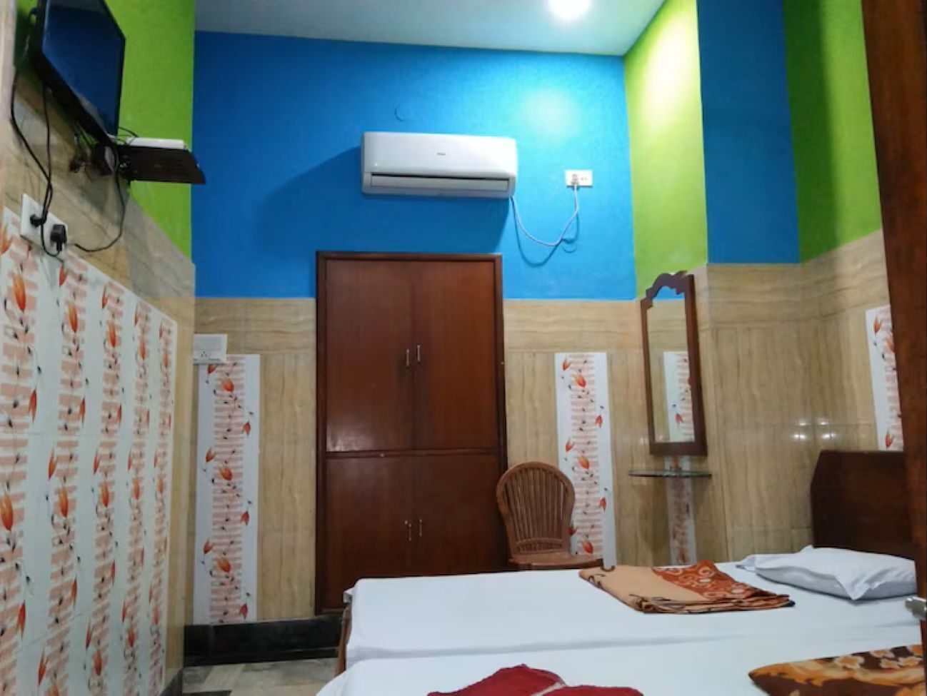 A bedroom with a bed, a wardrobe, a chair, and an air conditioning unit.