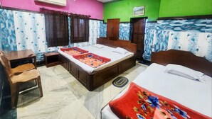A hotel room with two beds, a desk, a chair, an air conditioner, and a ceiling fan. - Hotel Sushil International (Kolkata)