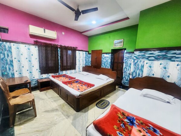 A hotel room with two beds, a desk, a chair, an air conditioner, and a ceiling fan. - Hotel Sushil International (Kolkata)