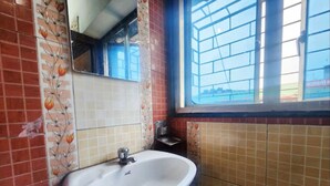A bathroom with a sink, tiled walls, a window, and a mirror. - Hotel Sushil International (Kolkata)