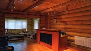 Ein Interieur einer Holzblockhütte mit einem Holzbüro, einem Kamin, einer Couch und einem Fenster mit Jalousien.