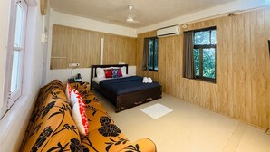 A bedroom with a bed, a sofa, wooden paneling, a window, and an air conditioning unit.