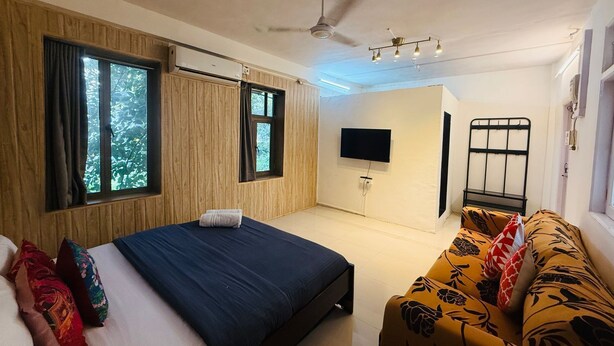 A bedroom with a bed, a sofa, a TV, and a ceiling fan.