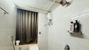 A small bathroom with a toilet, shower, and a shelf with toiletries.