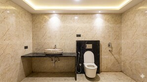 Un bany amb sòl de marbre, un lavabo amb una bassina decorativa, un vàter i una zona de dutxa.