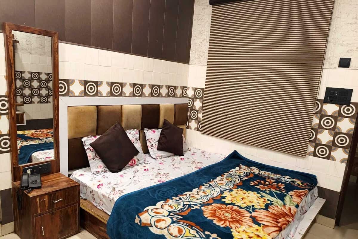 A bedroom with a bed, a bedside table, a mirror, and a window with blinds.